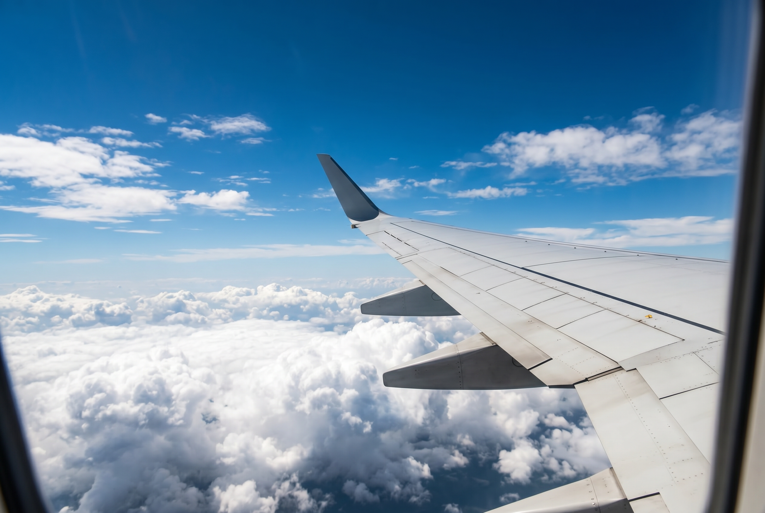 Airplane wing above clouds in bright blue daytime sky